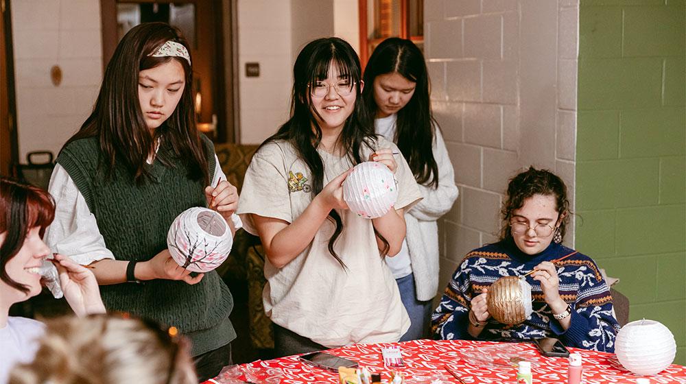 A group of students painting paper lanterns together at a table.